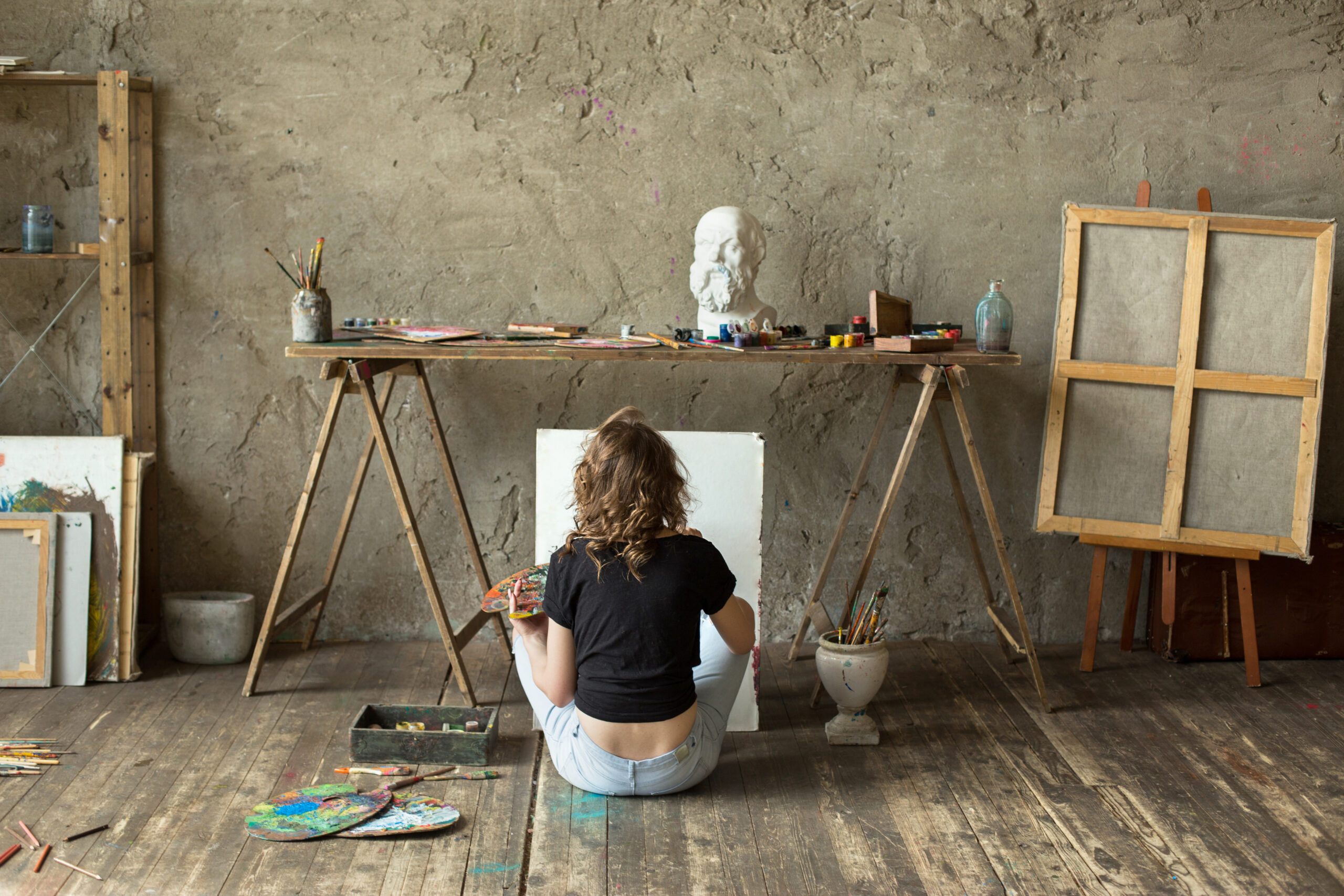 Woman painter sitting on floor with canvas