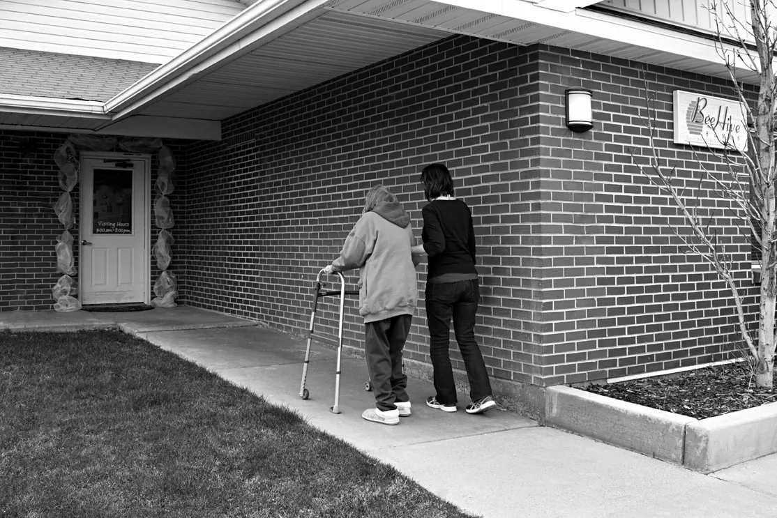 Photo of woman helping elderly woman to door of building. Katie Benson