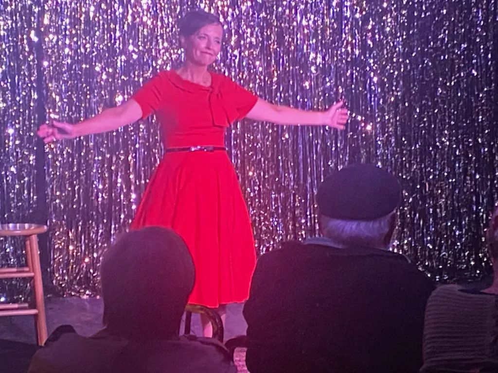 Brooke Schooley wearing a red dress performing Who Knows Where or When on a stage in front of a shiny curtain.