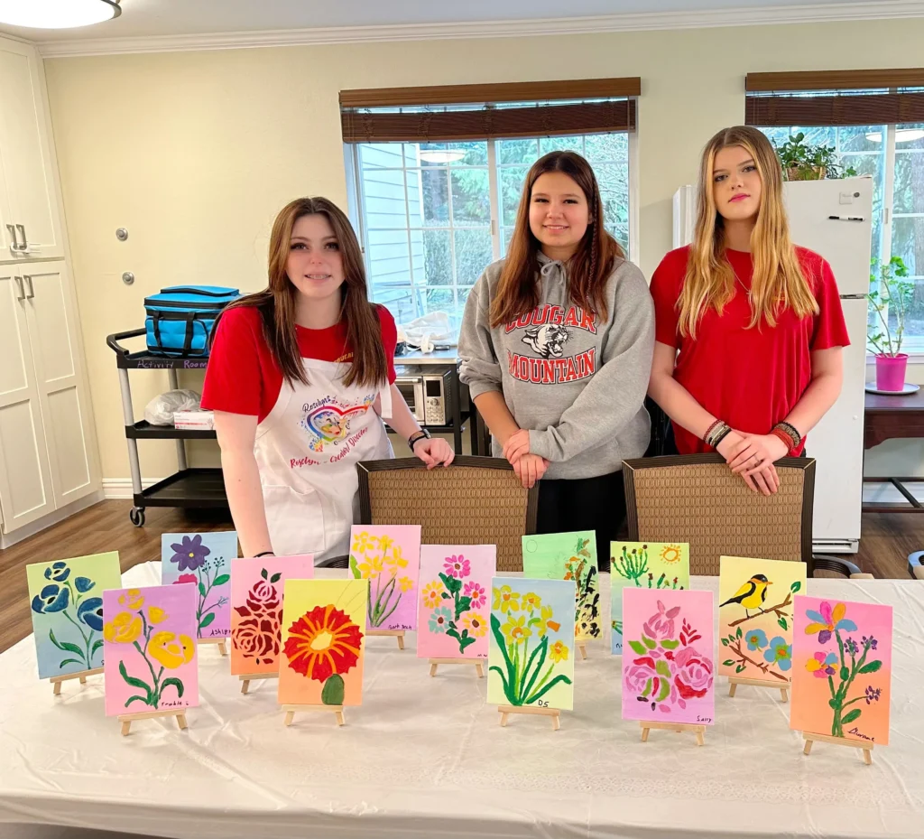 Roselyn and friends behind table of multiple finished canvases