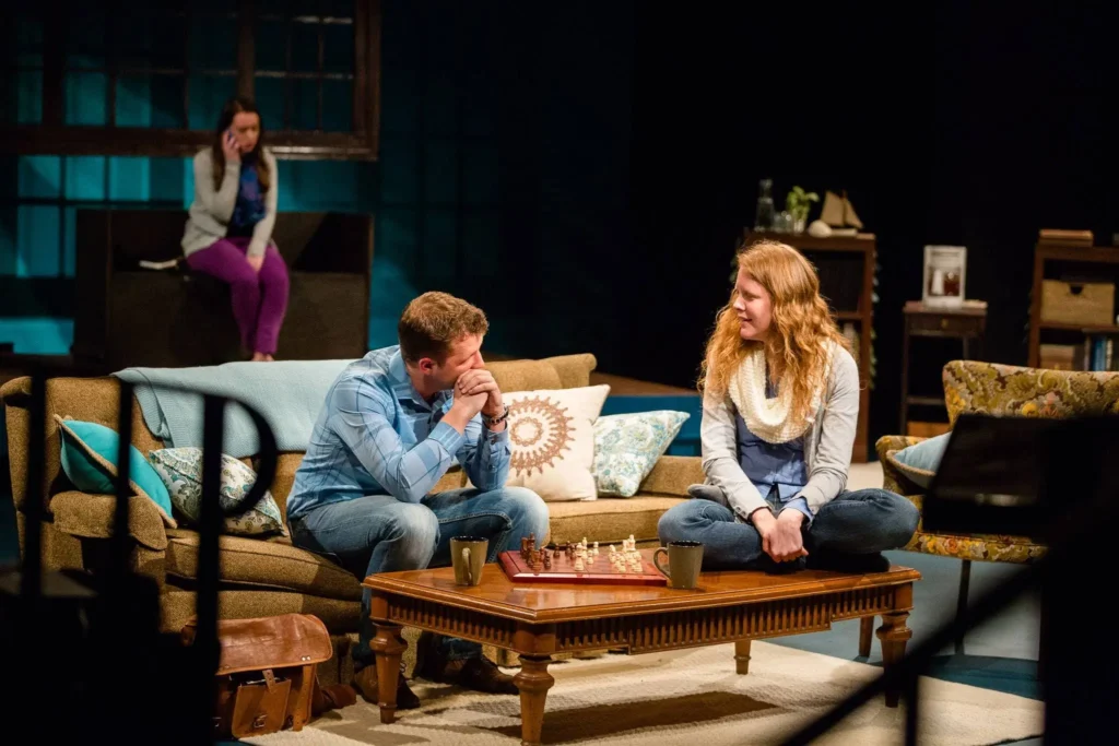 In the foreground, Dr. Erin Naler, playing Lilly Wilde, and Luke Hollis, playing Jonathan Lake. In the background, Janie Elizabeth Board, playing Brittany. In the scene, Jonathan is meeting with Lilly, his psychiatric patient, whose case (and his inability to solve it) takes over everything else as he becomes personally invested. In the background, Brittany attempts to maintain her romantic relationship with Jonathan, who doesn't answer his phone.