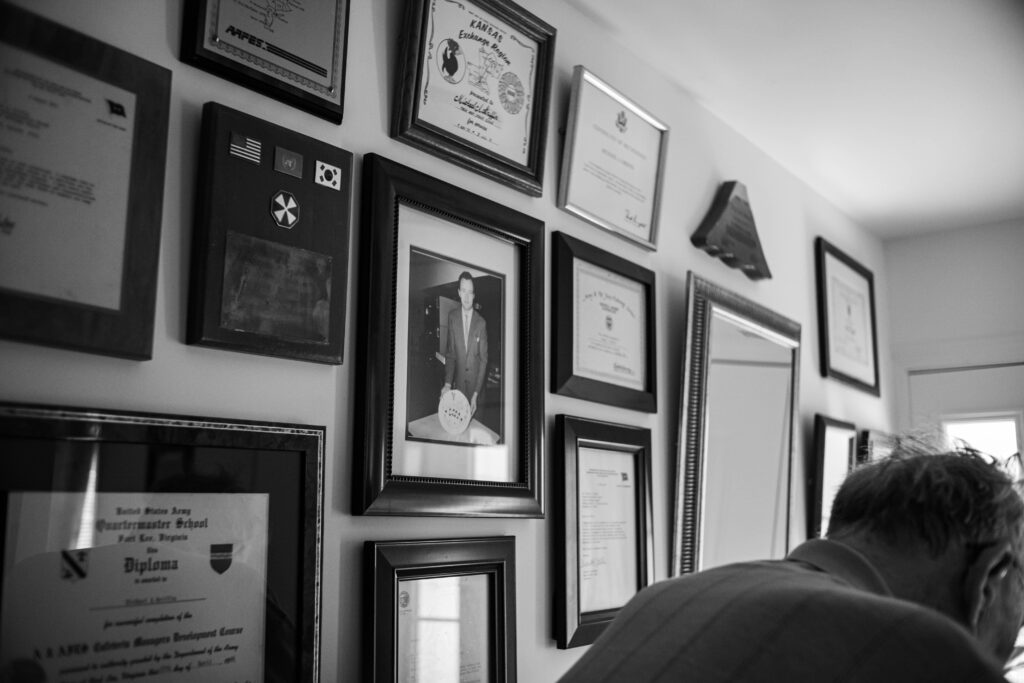 As Dad slowly shuffles his way through the house and into the kitchen, he passes by the awards, certifications, and commendations he earned over decades of service, traveling the world with the U.S. government. In the center of it all hangs a 33-year-old portrait of him in his prime—a reminder of the man he was and the legacy of hard work and dedication he left behind. Once filled with stories of his travels, history, and politics—subjects he loved—the halls have grown quieter with the onset of dementia. Now, his accomplishments silently speak for him.