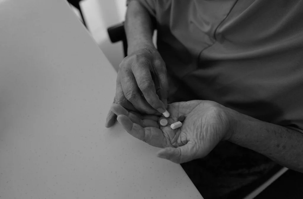 As part of her morning routine in 2024, E. Holi takes her medicine independently as prepared by her caregiver.