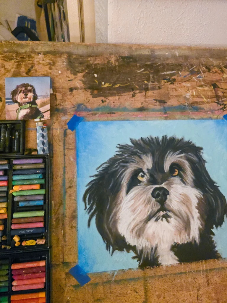 Painting of a short-haired dog breed in progress, with pencils, paint, and a reference photo. 