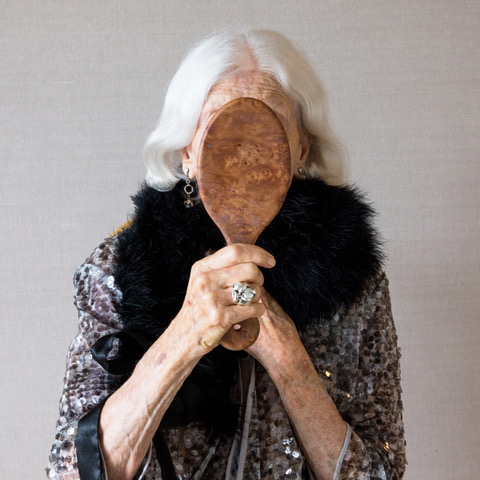 Jennifer Blau from her series "ForgetMeNot", that shows her face hidden by a handheld wooden mirror, reflective glass side turned away from viewer.