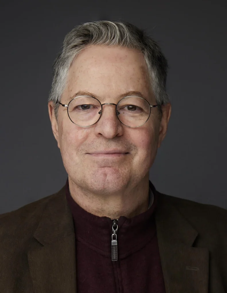 Headshot of John Beltzer in a dark suit atop a dark background.