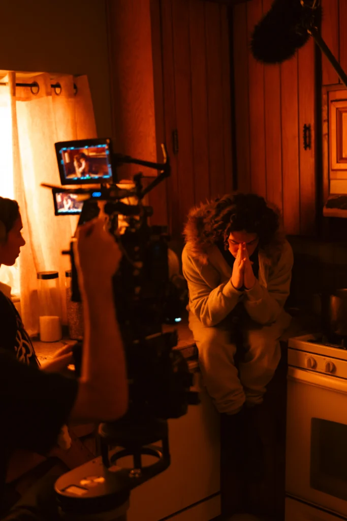 A young adult sits in the kitchen, hands pressed against their face, as they grapple with reality
