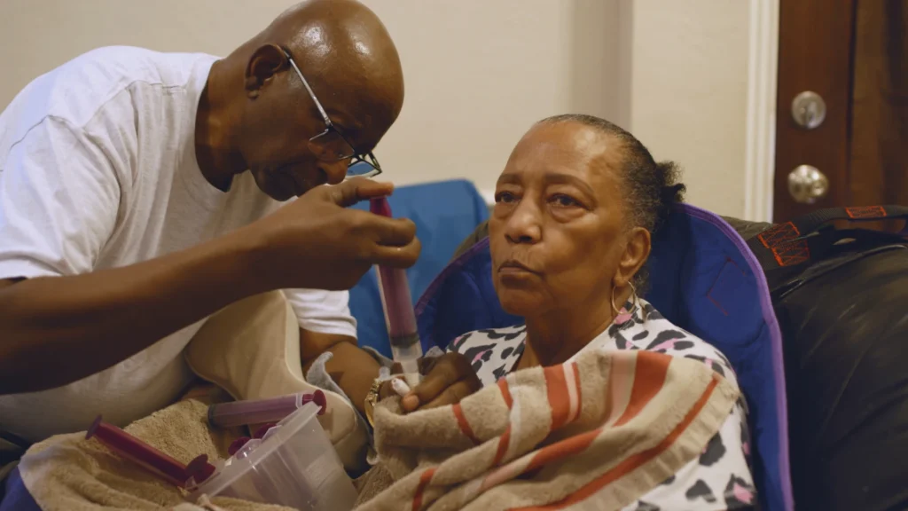 A man tends to his mother, who is wrapped in a blanket
