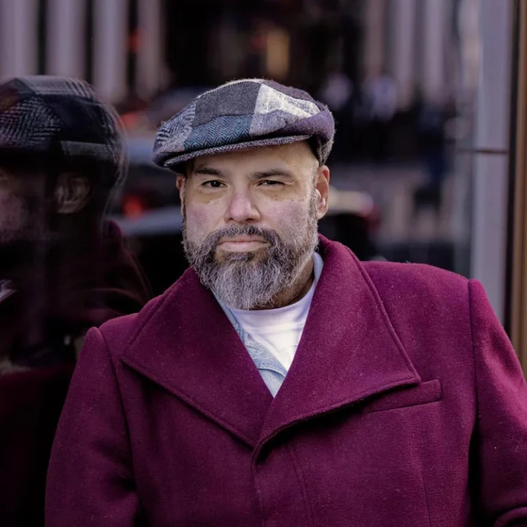 Russell leans against a shop window in a wine-colored jacket
