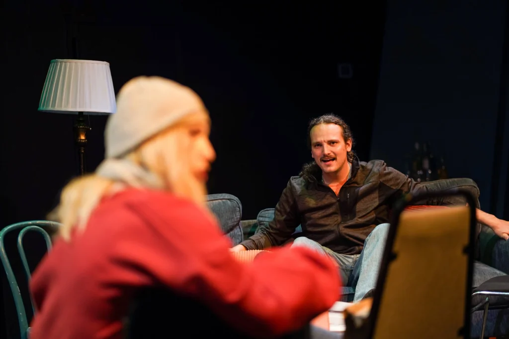 A man sitting on a couch expresses feelings of distress at an older woman in red