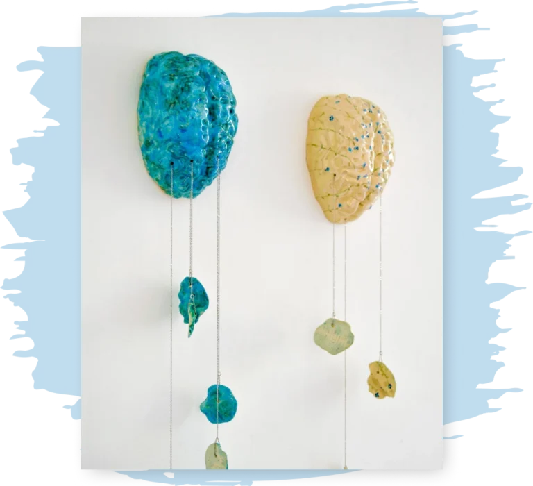 two ceramic brains hang from a wall, one blue one yellow, with pieces of the brain broken and hanging downward by chains.